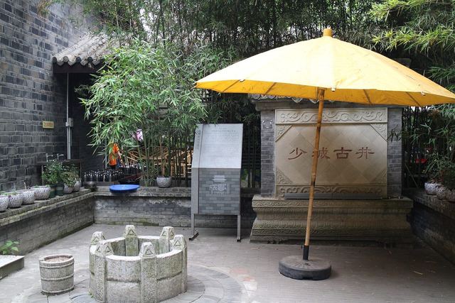 A stone well under a yellow parasol in a walled corner of People's Park