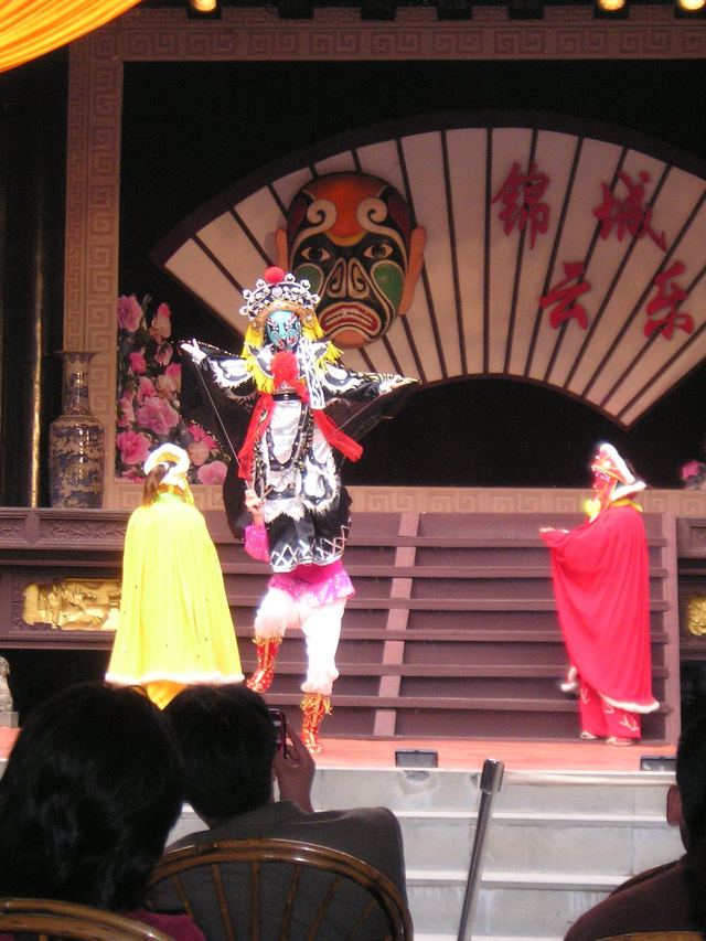 A masked performer in an embroidered costume on stage during a Sichuan opera show