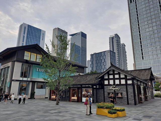 Low grey-roofed shops and glass storefronts at Taikoo Li, towers behind