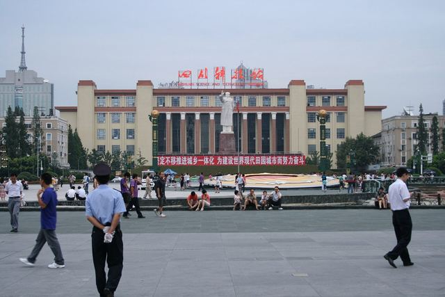 People crossing the wide paving of Tianfu Square, statue and exhibition hall behind